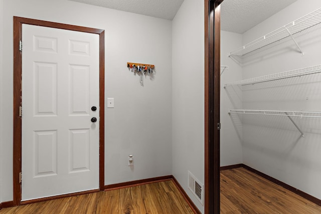 interior space featuring a textured ceiling, baseboards, visible vents, and wood finished floors