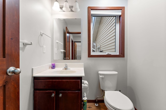 half bathroom featuring toilet, baseboards, and vanity