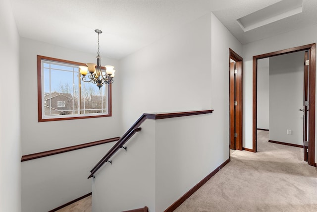 corridor featuring carpet flooring, a notable chandelier, baseboards, and an upstairs landing