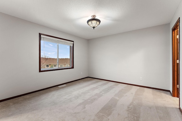 empty room with a textured ceiling, baseboards, light colored carpet, and visible vents