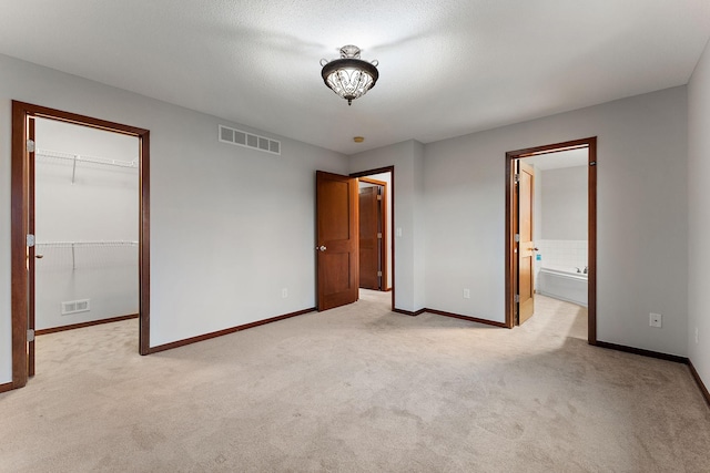 unfurnished bedroom featuring visible vents, light carpet, and a walk in closet