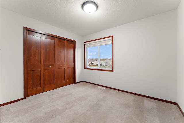 unfurnished bedroom with baseboards, light carpet, a closet, and a textured ceiling
