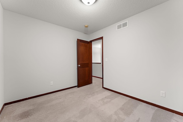 spare room with baseboards, light carpet, a textured ceiling, and visible vents