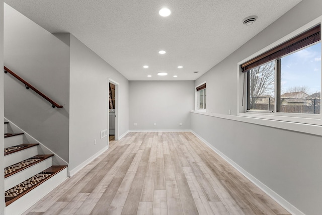 basement with a textured ceiling, visible vents, baseboards, light wood-style floors, and recessed lighting
