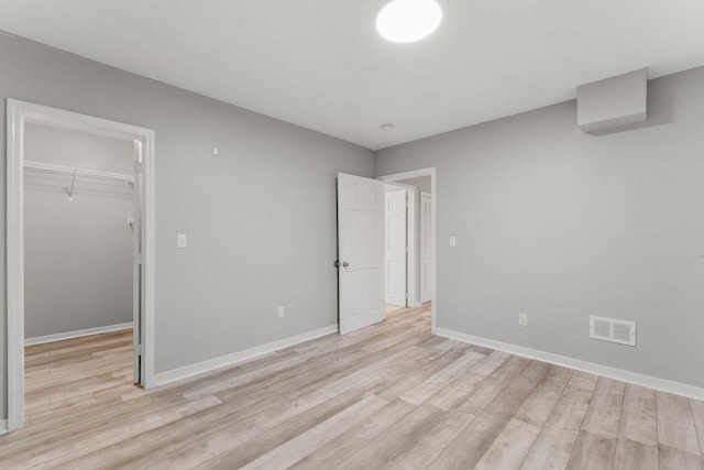 unfurnished bedroom featuring a spacious closet, a closet, light wood finished floors, and visible vents