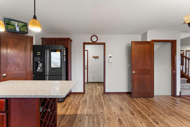 16268 Tahinka Ct NW, Prior Lake, MN 55372 - kitchen featuring black refrigerator with ice dispenser, light countertops, light wood-type flooring, decorative light fixtures, and a kitchen bar
