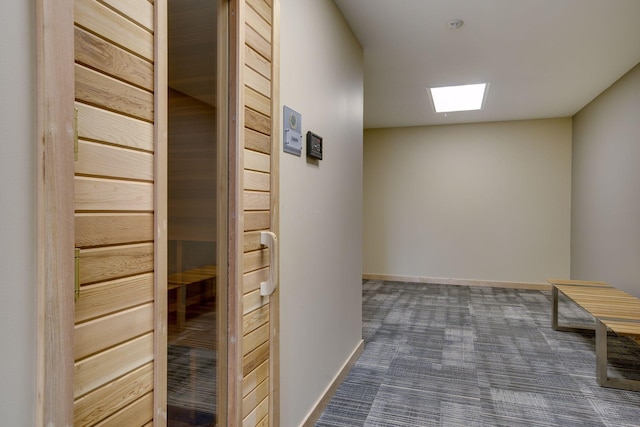 hall featuring dark colored carpet, baseboards, a sauna, and a skylight