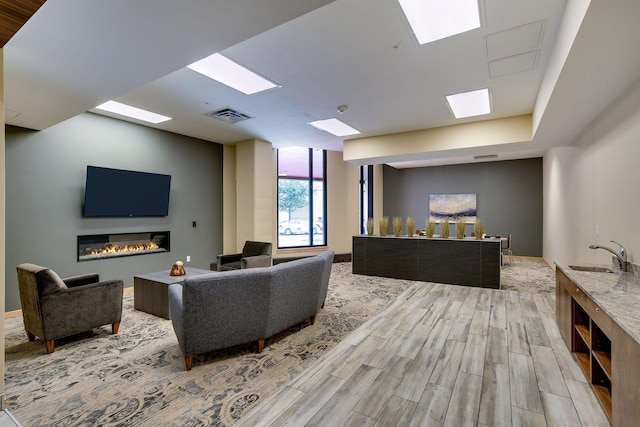 living area with a glass covered fireplace, a skylight, wood finished floors, and visible vents