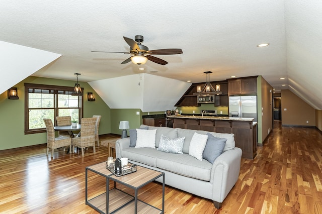 living room featuring a ceiling fan, lofted ceiling, wood finished floors, a chandelier, and baseboards