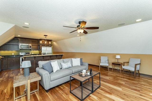living area featuring vaulted ceiling, light wood-type flooring, a ceiling fan, recessed lighting, and a textured ceiling