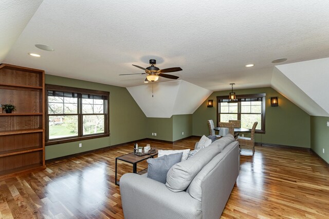 living room featuring vaulted ceiling, wood finished floors, a textured ceiling, ceiling fan, and baseboards