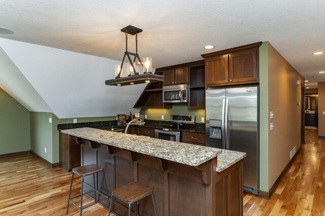 kitchen featuring appliances with stainless steel finishes, light wood-type flooring, baseboards, a kitchen bar, and light stone counters