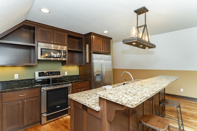 kitchen featuring appliances with stainless steel finishes, open shelves, a sink, light wood-style flooring, and a kitchen island with sink