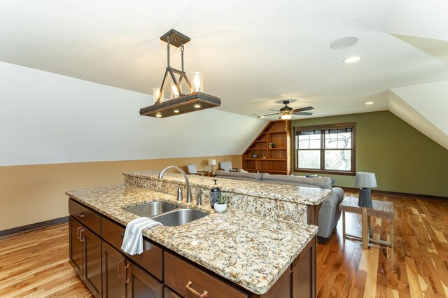 kitchen with a sink, vaulted ceiling, ceiling fan, light wood finished floors, and light stone countertops