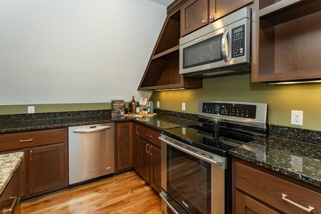 kitchen featuring stainless steel appliances, light wood-type flooring, and dark stone countertops