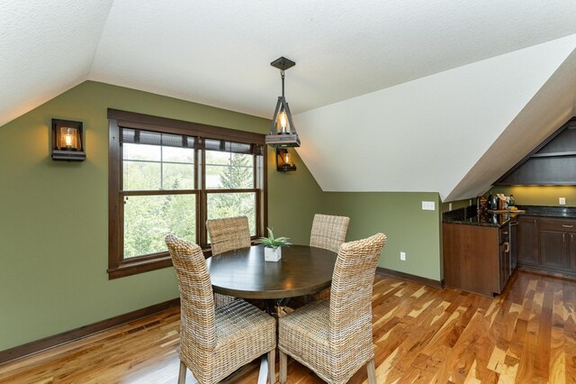 dining space featuring vaulted ceiling, baseboards, and light wood-style floors