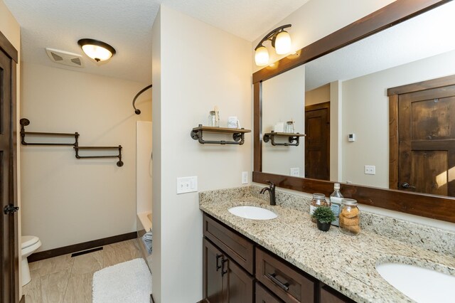 bathroom with toilet, double vanity, shower / washtub combination, and baseboards