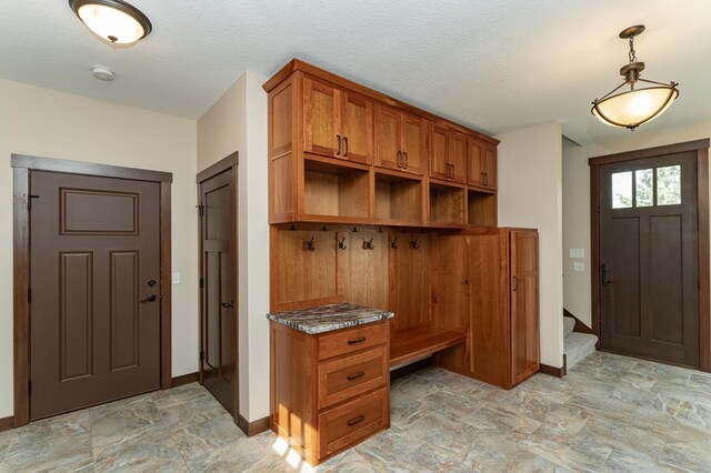 mudroom featuring baseboards, built in desk, stone finish floors, and a textured ceiling