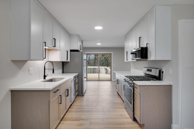 kitchen featuring appliances with stainless steel finishes, a sink, light countertops, light wood-style flooring, and recessed lighting