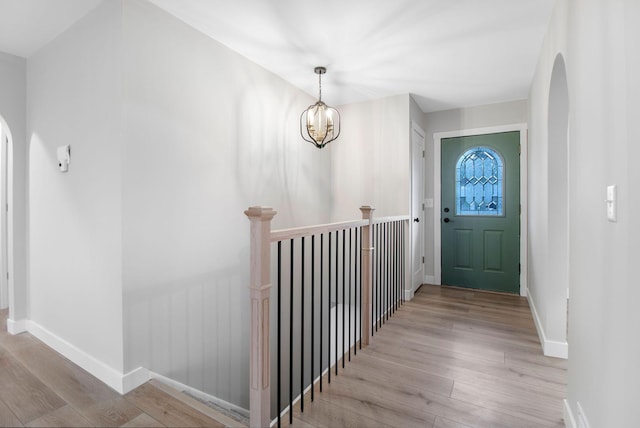 entryway featuring light wood-style floors, arched walkways, baseboards, and a notable chandelier