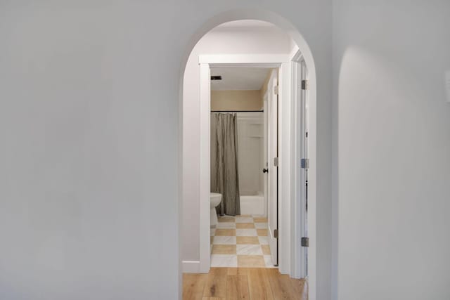 hallway featuring arched walkways and light wood-type flooring