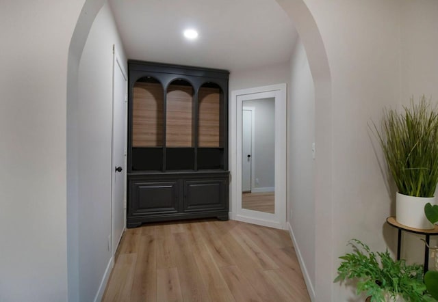 hallway with baseboards, arched walkways, and light wood-style floors