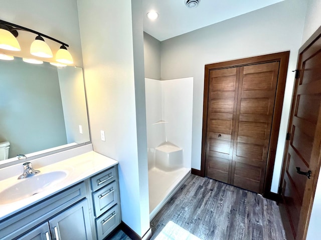 bathroom with baseboards, toilet, walk in shower, vanity, and wood finished floors
