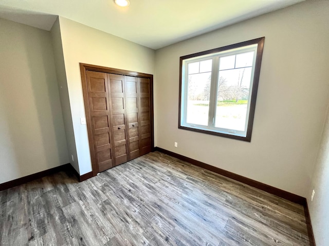 unfurnished bedroom with a closet, wood finished floors, baseboards, and recessed lighting