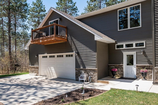 view of front of house with a balcony, stone siding, a garage, and driveway