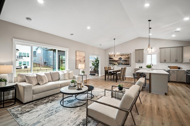 living area featuring baseboards, a chandelier, lofted ceiling, and light wood-style floors