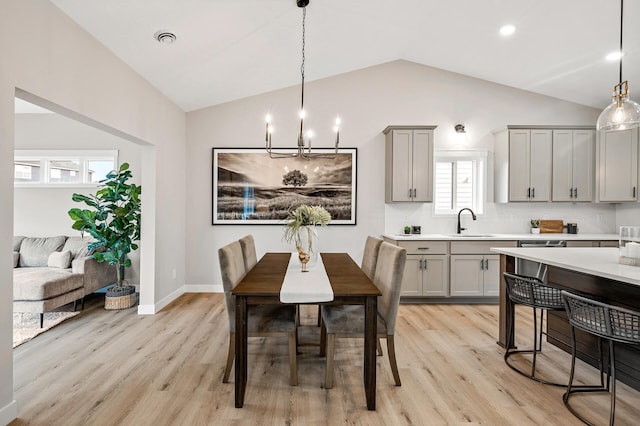 dining area with light wood-type flooring, a notable chandelier, vaulted ceiling, and visible vents