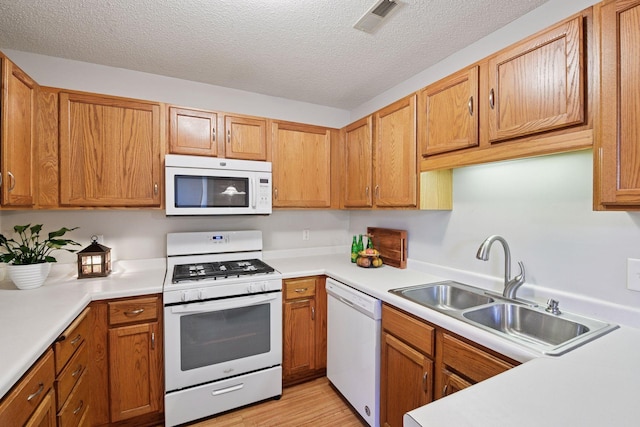kitchen featuring visible vents, a sink, white appliances, and light countertops
