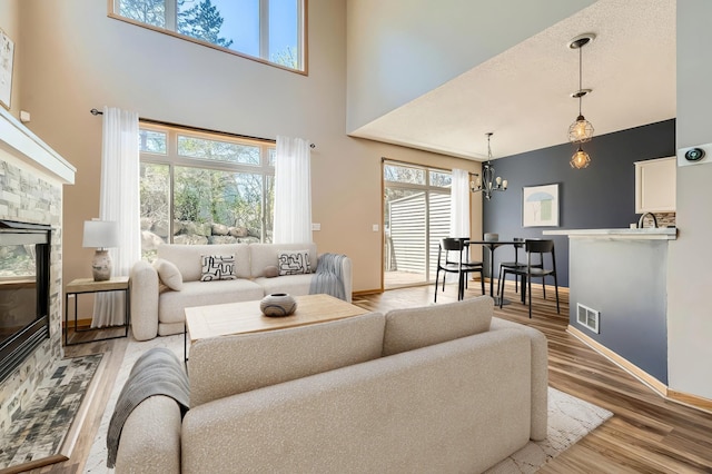 living room with a towering ceiling, a chandelier, light wood finished floors, healthy amount of natural light, and a stone fireplace