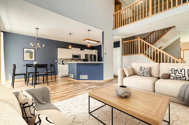 living area with light wood-type flooring, a chandelier, stairway, baseboards, and a high ceiling