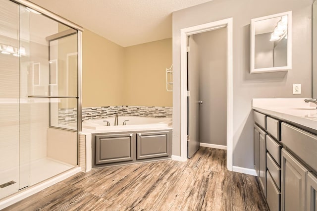 bathroom featuring a stall shower, wood finished floors, a garden tub, vanity, and baseboards