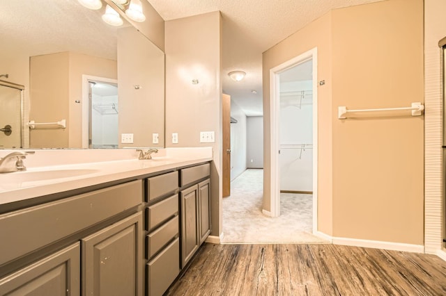 full bath featuring wood finished floors, a textured ceiling, double vanity, a walk in closet, and baseboards