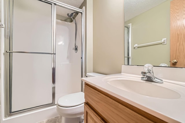 bathroom featuring a textured ceiling, a stall shower, toilet, and vanity