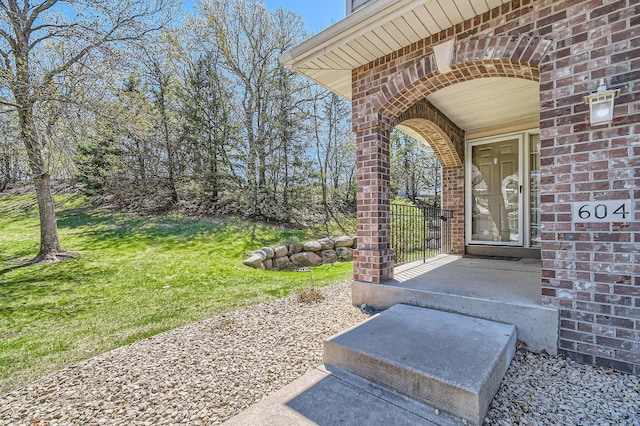 view of exterior entry with brick siding and a lawn