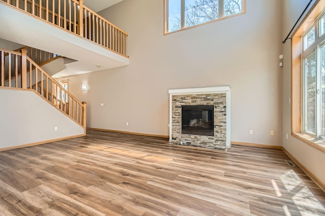 unfurnished living room with a towering ceiling, stairs, wood finished floors, baseboards, and a fireplace