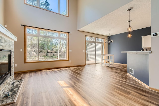 unfurnished living room with a towering ceiling, a chandelier, light wood-style flooring, a stone fireplace, and baseboards