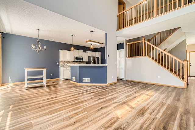 unfurnished living room with a chandelier, light wood-type flooring, stairs, baseboards, and a high ceiling