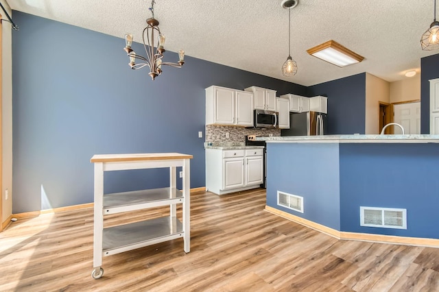 kitchen featuring appliances with stainless steel finishes, a textured ceiling, white cabinetry, a chandelier, and light wood finished floors