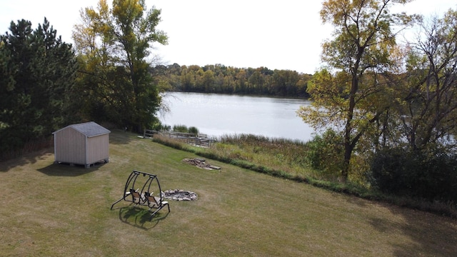 view of yard featuring a forest view, an outbuilding, a shed, an outdoor fire pit, and a water view