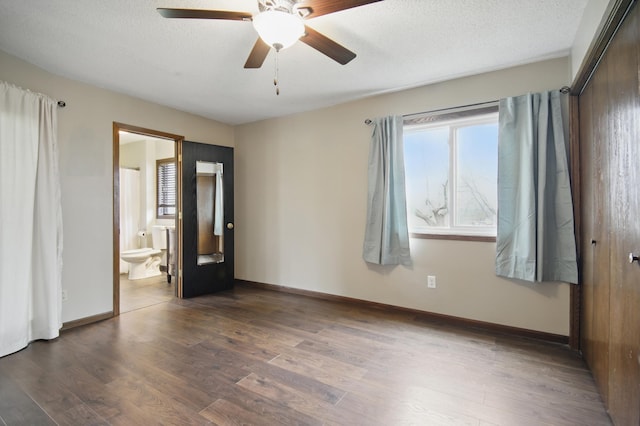 unfurnished bedroom featuring multiple windows, connected bathroom, and wood finished floors