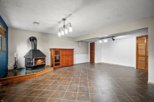 unfurnished living room featuring a wood stove, visible vents, a textured ceiling, and track lighting