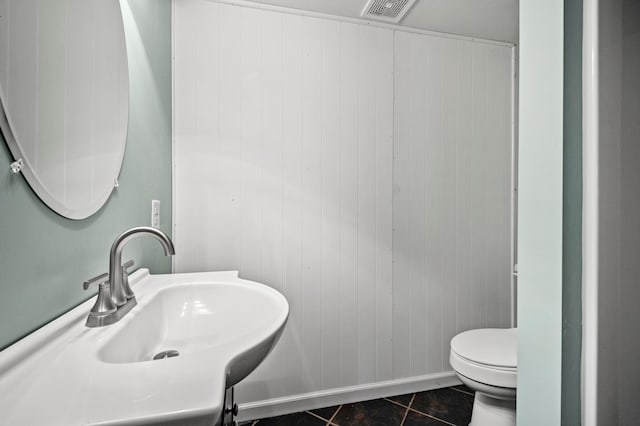 bathroom featuring a sink, toilet, visible vents, tile patterned flooring, and wooden walls