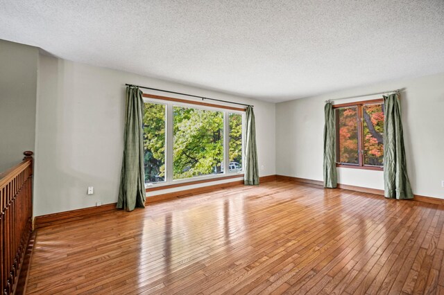 unfurnished room with a textured ceiling, wood-type flooring, and baseboards