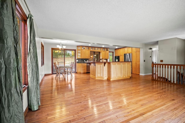 unfurnished living room with a textured ceiling, a chandelier, light wood-style floors, and baseboards