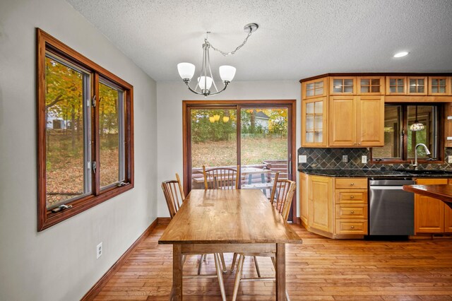 kitchen featuring stainless steel dishwasher, light wood-style floors, dark countertops, a textured ceiling, and a chandelier