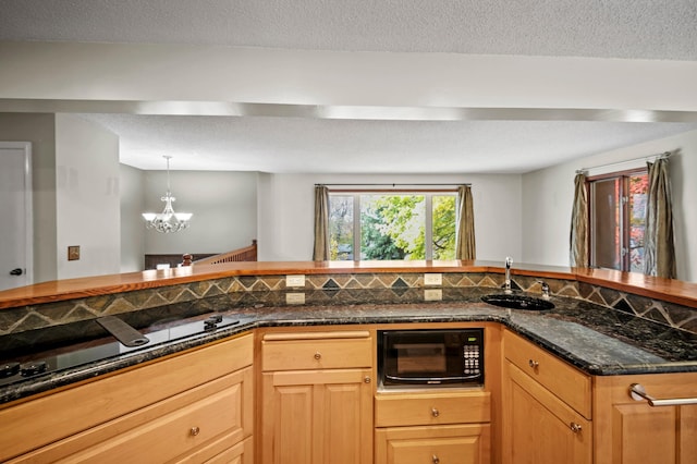 kitchen featuring black appliances, a sink, a chandelier, dark stone countertops, and decorative light fixtures